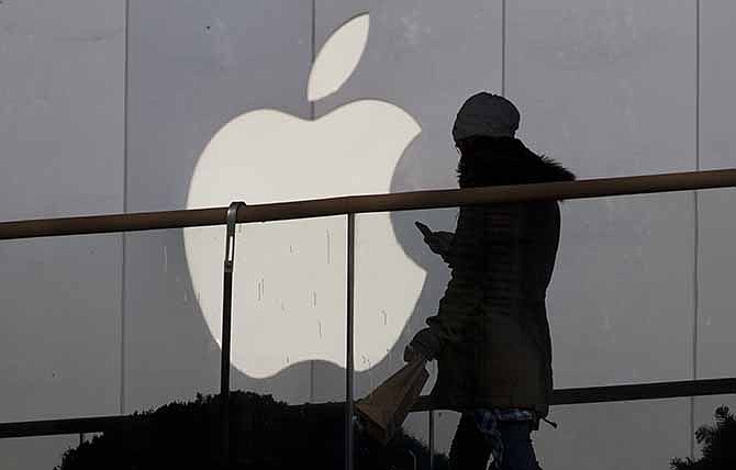 In this Dec. 23, 2013 file photo, a woman using a phone walks past Apple's logo near its retail outlet in Beijing. 