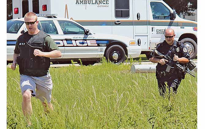 Drug Task Force Detective Josh Talbott, left, and Jonesboro Police Department Patrolman First Class Duane Busby run across a field adjacent to Moore Road while responding to a Saturday, May 3, 2014 shooting in Jonesboro, Ark.