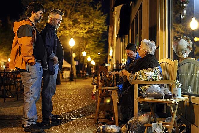 Dan Stark, left, and Stephen Ellison stop and chat with Donna Felsheim, right, and Chris Durrill as the two sit and spin wool during Friday night's downtown Art Stroll in Jefferson City.
