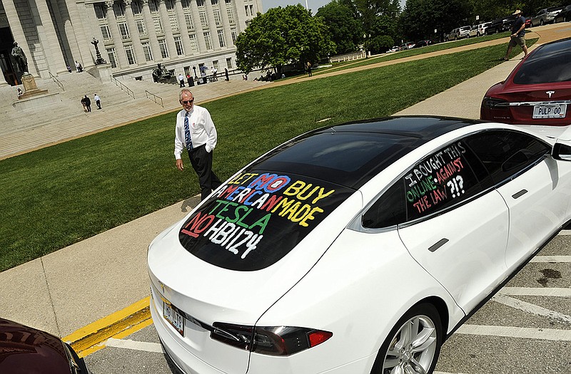 A passerby reads a PROTEST message written on the windows of a Tesla Model S as he walks by a row of the electric cars parked in front of the Capitol on Monday afternoon. 