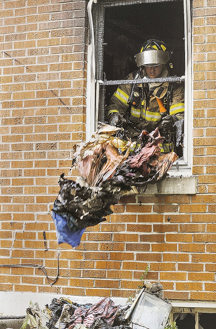  Jefferson City firefighter, Anthony Trapani, tosses smoldering clothing out the window in an effort to make sure the fire does not reignite Monday after firefighters doused the blaze at 1024 Hawthorne Pkwy. It took the crew of more than a dozen nearly 45 minutes to knock down flames and have the fire under control. 