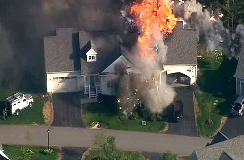 In this frame grab from television helicopter video, a police SWAT team, left, is parked on the lawn of a home in Brentwood, N.H., as it explodes in flames Monday. Shots were fired just before the fire.