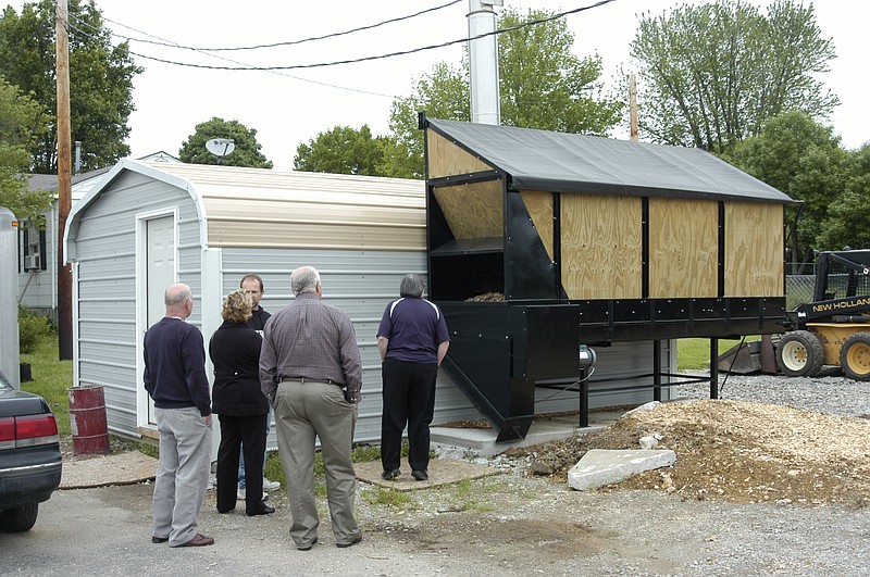 Steve Bonecutter shows several members of the MRED the heating system installed at the new location of Bonecutter Body Shop and Beta Motorcycles. Sawdust is put into the top of the bin on the right, taken by auger to a wood burning furnace inside the metal building. Then the water heated through a heat-exchange system is piped into the building.