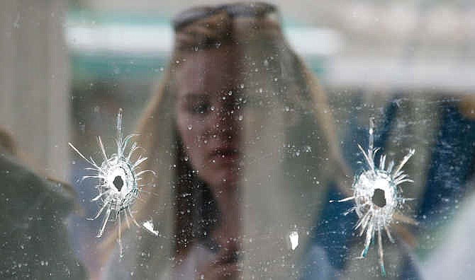 A woman looks at the bullet holes on the window of IV Deli Mark where Friday night's mass shooting took place by a drive-by shooter on Saturday, May 24, 2014, in Isla Vista, Calif. The shooter went on a rampage near a Santa Barbara university campus that left seven people dead, including the attacker, and seven others wounded, authorities said Saturday. 