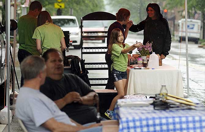 Olivia Anderson, center, catches rainwater as it falls from the canopy covering Three Story Coffee's table as vendors begin to pack up their wares at the conclusion of Lincoln University's farmers market on Madison Street on Saturday.