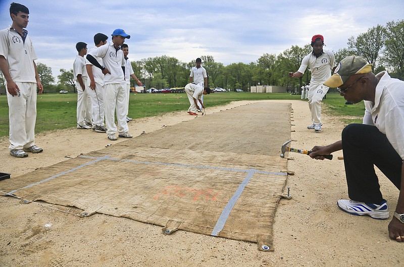 A sand and gravel cricket pitch is covered with a mat being hammered into the ground before a cricket match between Public School Athletic League (PSAL) teams John Adams and Midwood high schools, at Marine Park in the Brooklyn borough of New York.