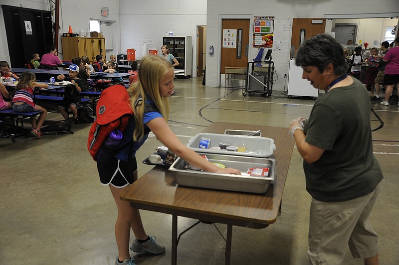 Fifth-grader Madalyn Benne grab a second cup of juice from the "share table" at breakfast Tuesday before Russellville Elementary summer school while Anne Brennecke welcomes her to school.