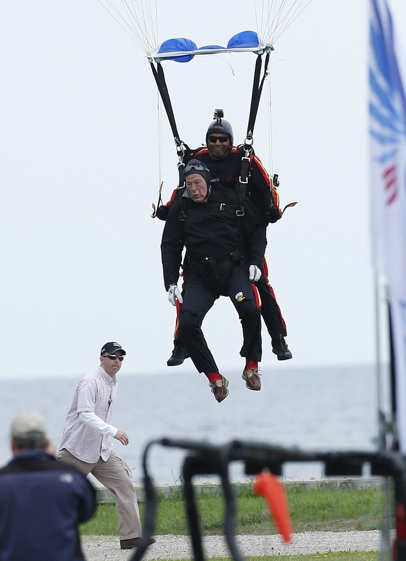 Former President George H.W. Bush, strapped to Sgt. 1st Class Mike Elliott, a retired member of the Army's Golden Knights parachute team, preapre to land on the lawn at St. Anne's Episcopal Church while celebrating Bush's 90th birthday in Kennebunkport, Maine on Thursday.