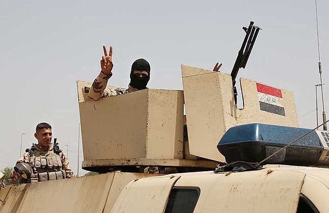 An Iraqi soldier flashes a V for victory sign while Iraqi men gather outside of the main army recruiting center to volunteer for military service in Baghdad, Iraq, Thursday, June. 12, 2014, after authorities urged Iraqis to help battle insurgents.