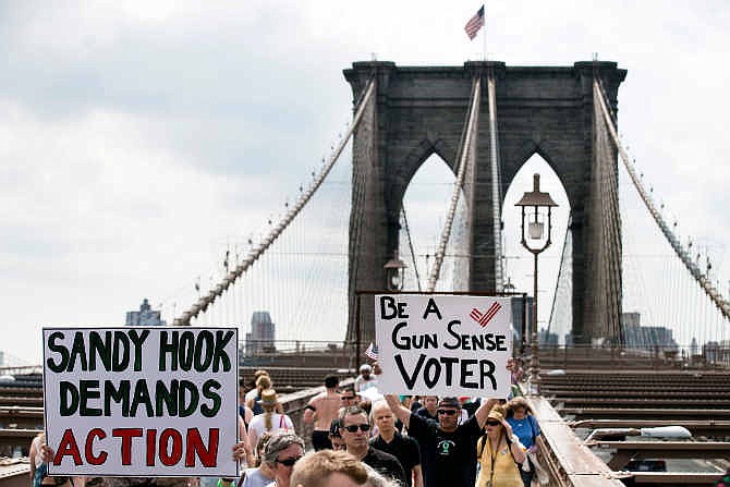 Demonstrators raise posters as they march across the Brooklyn Bridge to call for tougher gun control laws, Saturday, June 14, 2014, in New York. The protest was underwritten by former New York Mayor Michael Bloomberg, one of the most visible gun control advocates in the U.S., and included relatives of some of those slain in the 2012 shooting rampage at Sandy Hook Elementary School in Newtown, Conn.