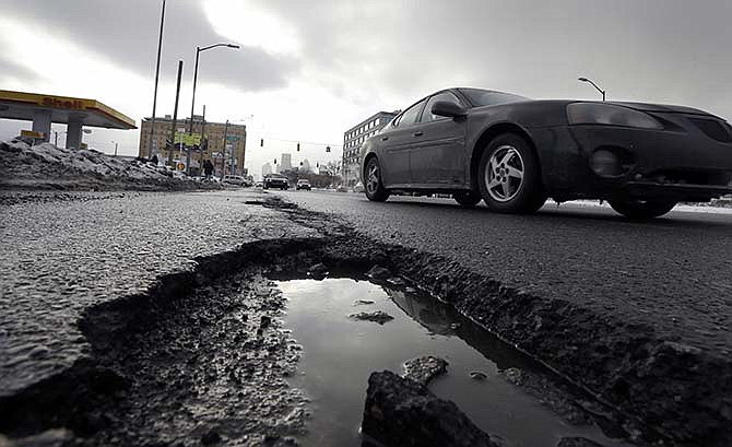 In this Feb. 11, 2014 file photo, a car drives by a pothole in Detroit.