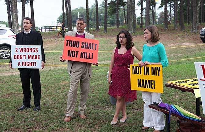 Joseph Shippen, far left, Assistant Rector of the Christ Episcopal Church in Macon, Ga., and Episcopal Bishop Rob Wright, second from left, stand with protestors outside the grounds of the Georgia Diagnostic and Classification Prison in Jackson, Ga., before the scheduled execution of Georgia death row inmate Marcus Wellon on Tuesday June 17, 2014. 