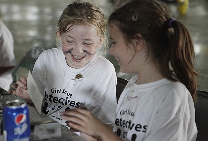 Jessica Koenigsfield, 9, left, laughs with Arica Ketcherside, 9, while they attempt to transfer their fingerprints from an object like a soda can to paper at the Girl Scout event Mysteries After Dark at the Jaycee Fairgrounds. 