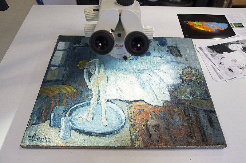 "The Blue Room," one of Pablo Picasso's first masterpieces sits under a microscope at The Phillips Collection, on Tuesday, in Washington. Scientists and art experts have found a hidden painting beneath the painting. Advances in infrared imagery reveal a bow-tied man with his face resting on his hand, with three rings on his fingers.