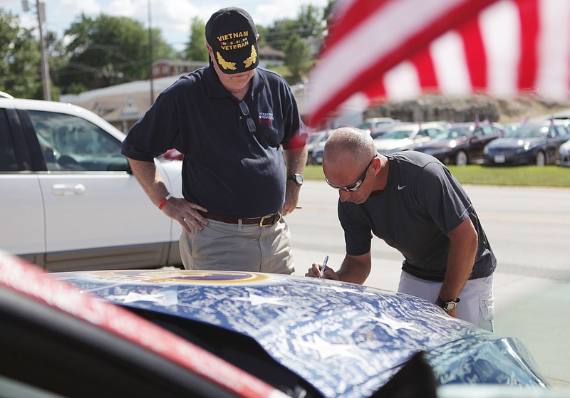 Dane Huffman (right) signs the Wounded Warriors Family Support Mustang while Lieutenant General John Sylvester (left) watches Tuesday at the Joe Machens Ford parking lot.