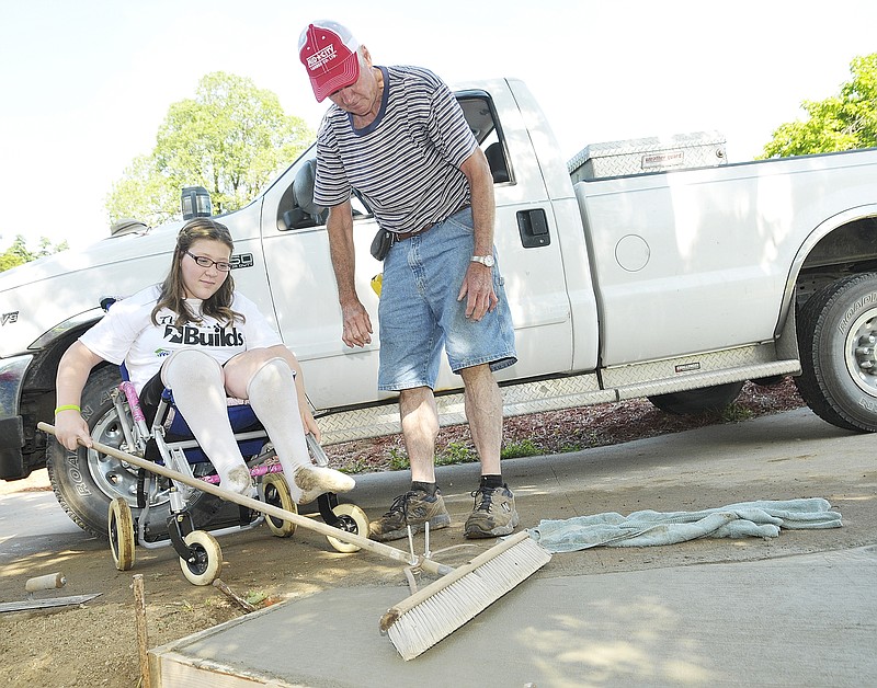 Norb Kolb directs Grace Fender as she pulls the broom across the concrete pad that will serve as the entry to the ramp under construction as her S. Country Club Drive home. Kolb is a volunteer helping to construct a ramp for Fender, who has spina bifida and has been in a wheelchair from very early childhood. The Lawson Elementary School fifth grade student will have surgery in July and after two months of extensive therapy, should be able to walk with the aid of a walker and eventually on her own.