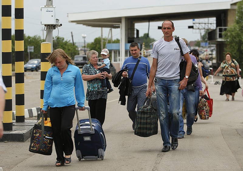 People carry their belongings as they walk to cross the border into Russia at the Ukrainian-Russian border checkpoint in Izvaryne, Luhansk region, eastern Ukraine. Thousands of Ukrainians in cars stuffed with belongings lined up Thursday at the eastern border to cross into Russia, with some saying they felt betrayed by their government and vowing never to return.