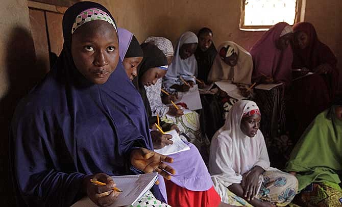 In this Monday, June 2, 2014 photo, Maimuna Abdullahi, left, writes down information from the blackboard as she and others attend school in Kaduna, Nigeria. Maimuna wore the scars of an abused woman anywhere: A swollen face, a starved body, and, barely a year after her wedding, a divorce. But for Maimuna, it all happened by the time she was 13. Maimuna is one of thousands of divorced girls in Nigeria who were married as children and then got thrown out by their husbands or simply fled.
