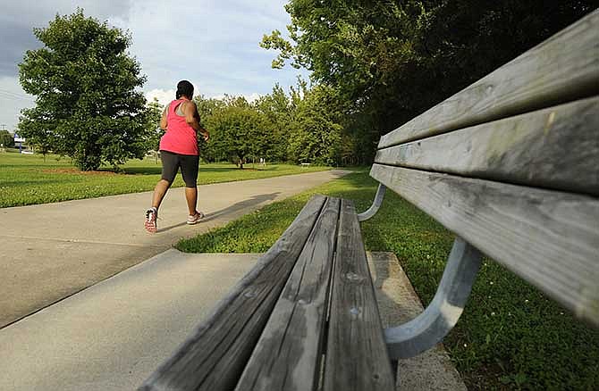 A jogger passes by a bench while enjoying the Jefferson City Greenway Trail along Edgewood Drive on
Wednesday afternoon, June 25, 2014.