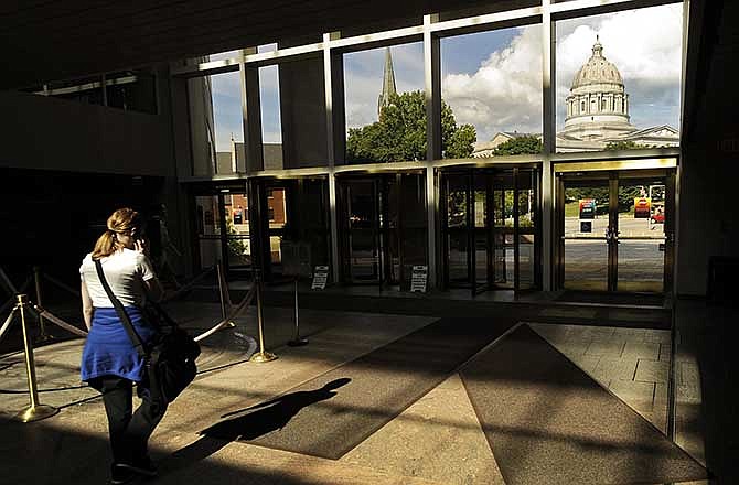 A state employee makes her way to the Truman Building's High Street entrance, with the reflection of the Missouri Capitol in the glass, at the end of the business day on Friday afternoon, June 27, 2014.