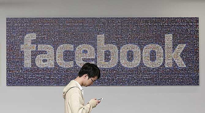 In this June 11, 2014 photo, a man walks past a Facebook sign in an office on the Facebook campus in Menlo Park, Calif. 