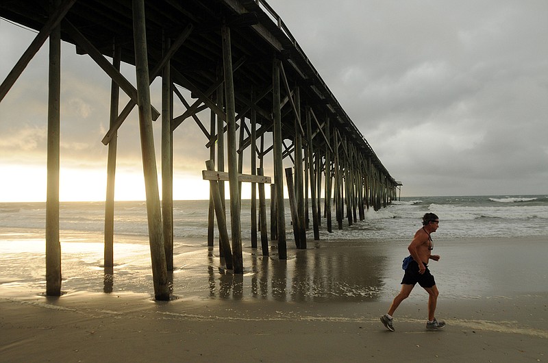 
Clouds and rain move in as a man jogs along the shore of the north end of Carolina Beach, North Carolina, Thursday.