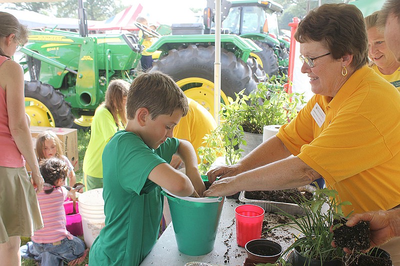 Thomas Harris, 10, Millersburg, makes a hole - with a little help from Master Gardener Anna Offutt - for a plant in his bucket garden Friday afternoon at the Callaway Youth Expo.