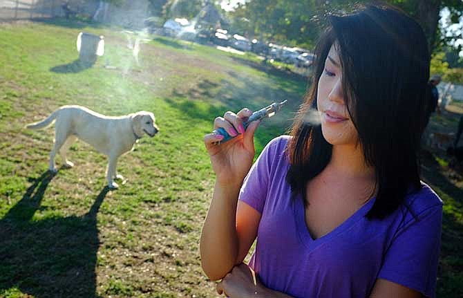 In this photo taken on Tuesday, July 1, 2014, Christine Choi takes a puff on her e-cigarette at a dog park in Los Angeles.