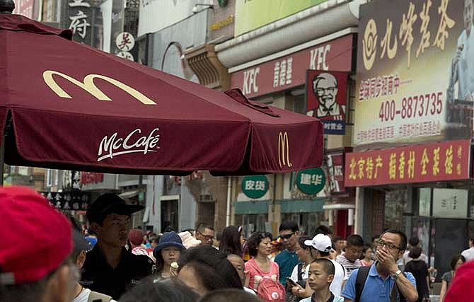 A man wipes his mouth near logos for McDonald's and KFC restaurants in Beijing Tuesday, July 22, 2014. China's food safety agency on Tuesday announced a nationwide inspection of processing factories and meat suppliers used by a company accused of selling expired beef and chicken to McDonald's and KFC.