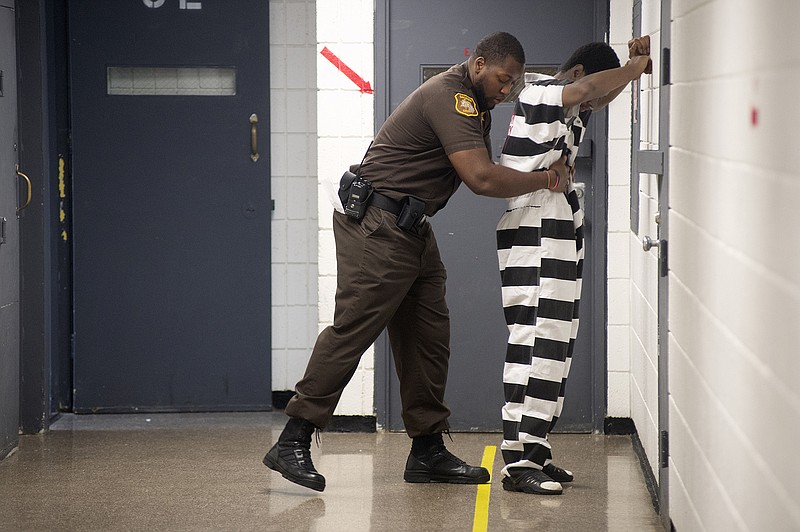 Corrections Officer Terence Moore frisks an inmate before the inmate meets with his attorney at the Saginaw County Jail, Friday, in Saginaw, Michigan. The Saginaw County Sheriff's Department has purchased new jumpsuits, with black and white stripes, for some of the inmates at the jail.