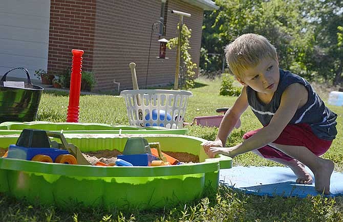 Jacob Mueller, 6, plays in the sandbox Thursday outside his new home in Stringtown. Jacob was adopted from Ukraine and arrived in the US on July 18.