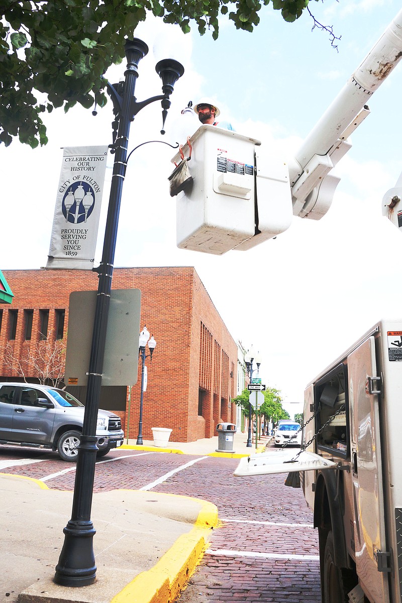 Micah Harris replaces a globe cover on the street lights on Court Street in downtown Fulton on Monday. The majority of the downtown street light covers have hail damage. The electric department is replacing the damaged globes throughout downtown Fulton.