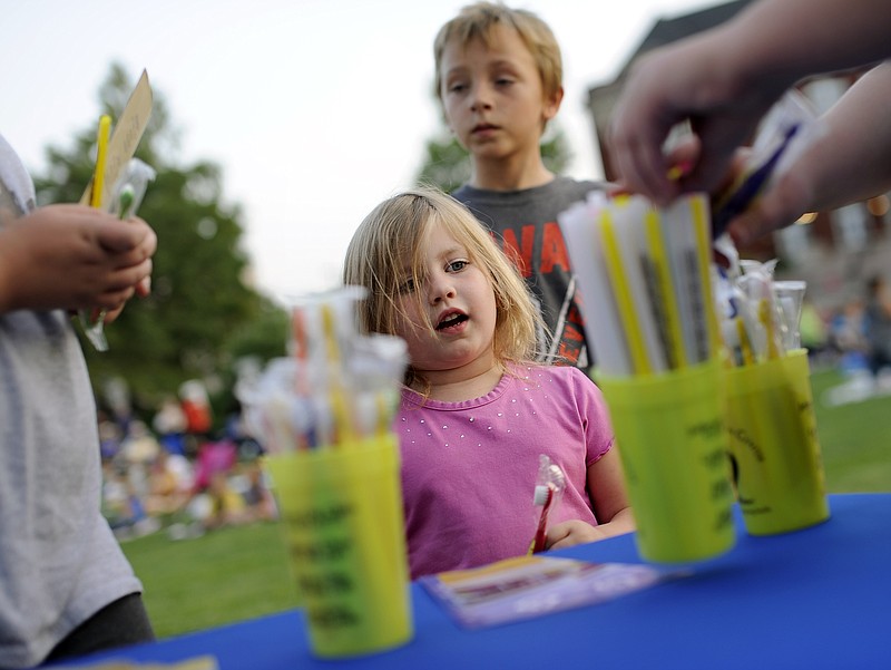 Lilly Bethel, center, and her brother Caleb Bethel, left, wait for their cousin Abby Farris, right, to pick out a color-changing mood straw as Community Health Center of Central Missouri representatives hand out free toothbrushes and straws before the start of Friday night's Stars Under the Stars movie night on the Missouri Capitol South Lawn. Community Health Center representatives were on hand for the event to pass out flyers and promotional material following the unveiling of their new mobile dentistry unit earlier in the evening.