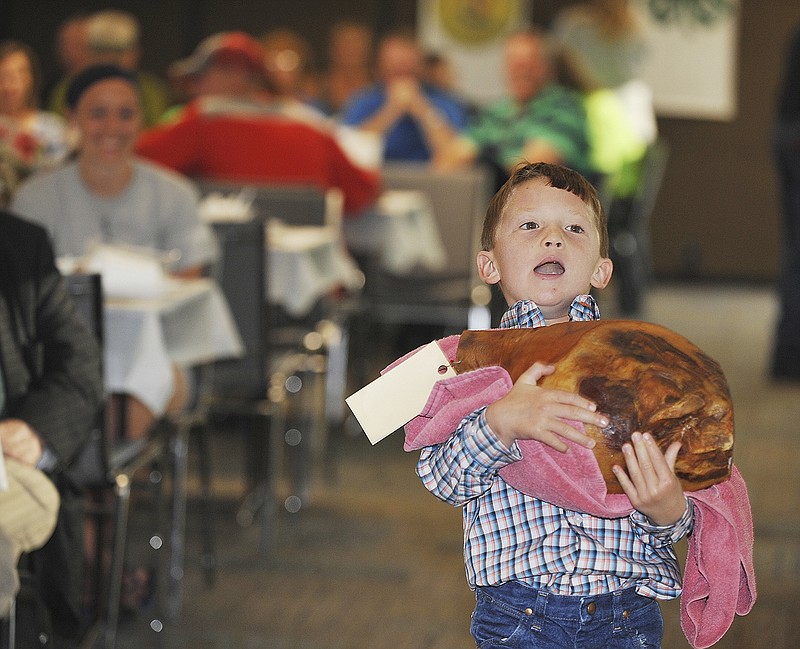 VonKingston Forck, 6, struggles to carry his ham in front of the crowd at Friday's annual Cole County Fair Ham Auction at Farm Bureau. He kept hoisting it up to his chin but eventually lost the battle as it rolled out of his hands on the last bid. The ham, that he himself cured with a little help from his dad and sister, brought a whopping $350. He is the son of Kelly and Teri Forck.