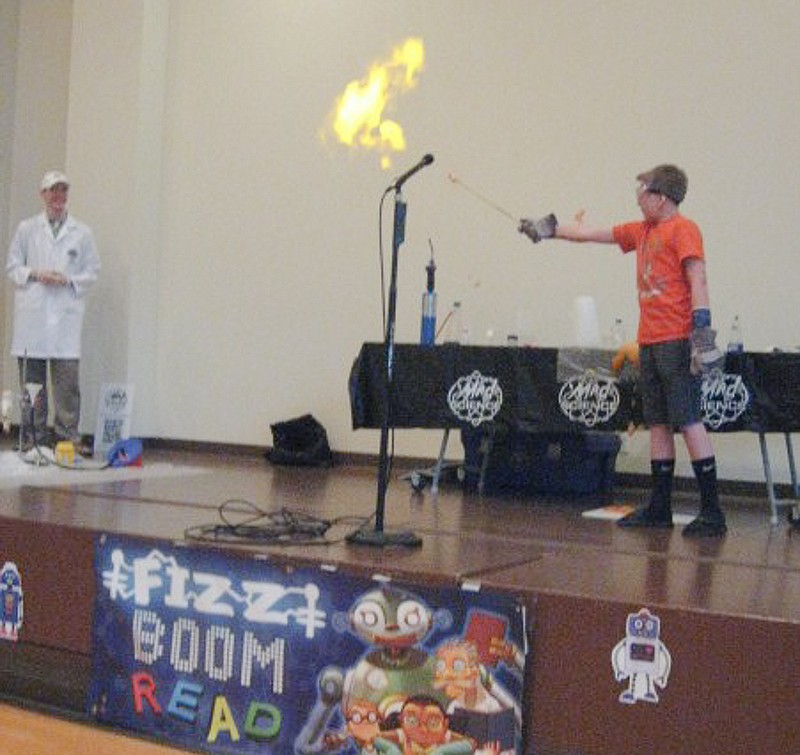 Flame erupts from a hydrogen-filled balloon held by a volunteer from the fifth through eighth grade group. The balloon was filled with hydrogen released during a demonstration of the release of hydrogen from hydrogen peroxide using aluminum foil. The presenter explained that if he had been putting on a magic show, no real information would have been given. Since this is science, each step was explained.