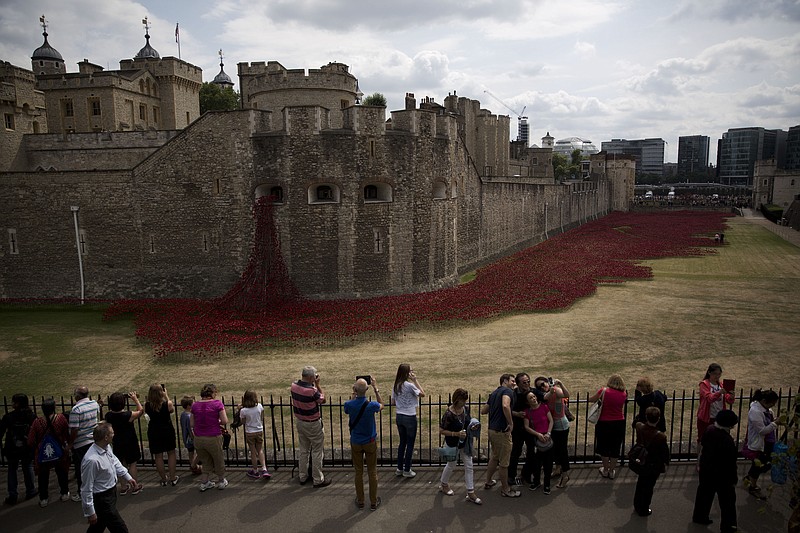 A group of people pose for a selfie backdropped by the ceramic poppy art installation by artist Paul Cummins entitled "Blood Swept Lands and Seas of Red' after its official unveiling in the dry moat of the Tower of London in London, Tuesday.  Britain's Prince William, his wife Kate Duchess of Cambridge and his brother Prince Harry visited the work in progress installation Tuesday to mark the centenary of World War I.