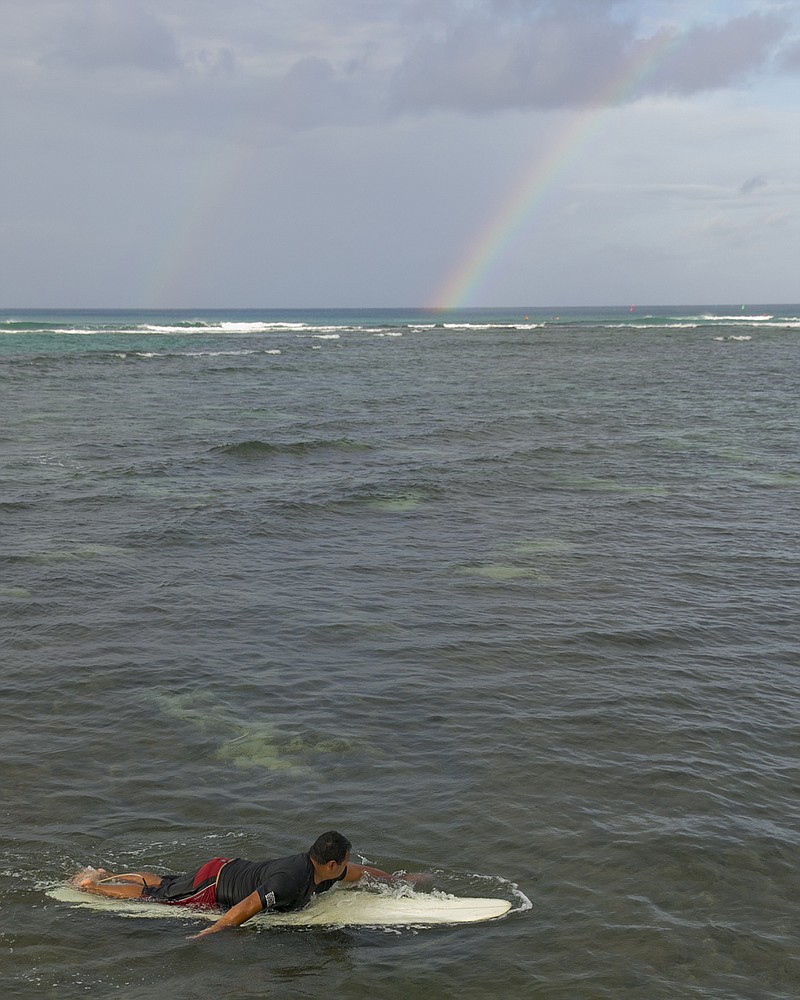 With a rainbow in the background, a surfer paddles to shore in Honolulu on Friday. Iselle came ashore early Friday as a weakened tropical storm, while Hurricane Julio, close behind it, strengthened and is forecasted to pass north of the islands.