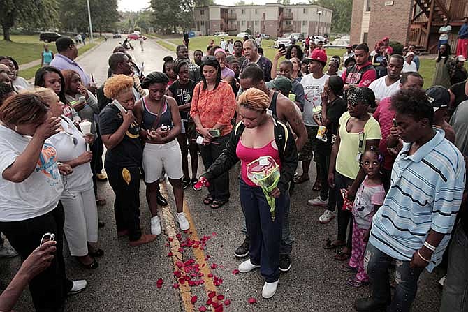 Lesley McSpadden, center, drops rose petals on the blood stains from her 18-year-old son Michael Brown who was shot and killed by police in the middle of the street in Ferguson, Mo., near St. Louis on Saturday, Aug. 9, 2014. McSpadden, told an acquaintance the shooting was "wrong and it was cold-hearted," the St. Louis Post-Dispatch reported. A spokesman with the St. Louis County Police Department, which is investigating the shooting at the request of the local department, confirmed a Ferguson police officer shot the man. The spokesman didn't give the reason for the shooting. 