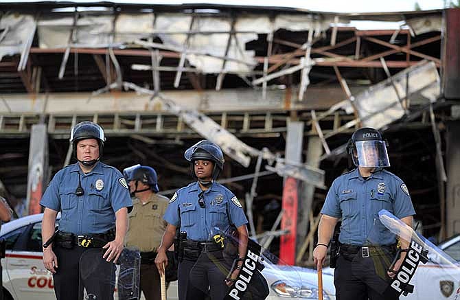 Police wearing riot gear stage outside the remains of a burned convenience store Monday, Aug. 11, 2014, in Ferguson, Mo. The FBI opened an investigation Monday into the death of 18-year-old Michael Brown, who police said was shot multiple times Saturday after being confronted by an officer in Ferguson. Authorities in Ferguson used tear gas and rubber bullets to try to disperse a large crowd Monday night that had gathered at the site of a burned-out convenience store damaged a night earlier, when many businesses in the area were looted.