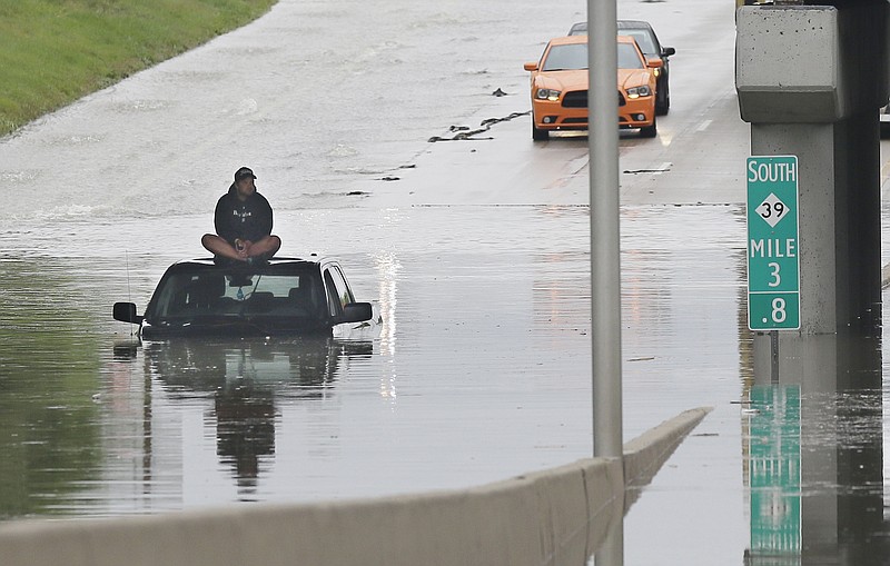 A stranded motorist sits on top his car as he awaits rescue from the flooded Southfield Freeway, Monday, in Dearborn, Mich. Heavy rain and thunderstorms left roads flooded and impassable.