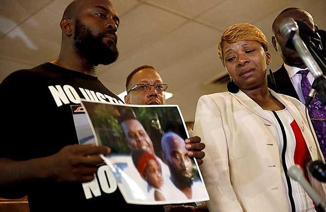 Lesley McSpadden, right, the mother of 18-year-old Michael Brown, watches as Brown's father, Michael Brown Sr., holds up a family picture of himself, his son, top left in photo, and a young child during a news conference Monday, Aug. 11, 2014, in Ferguson, Mo. Michael Brown, 18, was shot and killed in a confrontation with police in the St. Louis suburb of Ferguson, Mo, on Saturday, Aug. 9, 2014. 