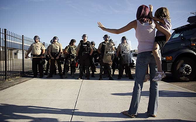 Protester Janelle Pittman holds her 6-year-old daughter, Kat, as police in riot gear stand guard in Ferguson, Mo. on Wednesday, Aug. 13, 2014. On Saturday, Aug. 9, 2014, a white police officer fatally shot Michael Brown, an unarmed black teenager, in the St. Louis suburb. 