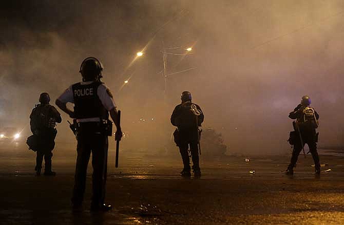 A law enforcement officer watches Sunday, Aug. 17, 2014, as tear gas is fired to disperse a crowd protesting the shooting of teenager Michael Brown last weekend in Ferguson, Mo. Brown's shooting in the middle of a street following a suspected robbery of a box of cigars from a nearby market has sparked a week of protests, riots and looting in the St. Louis suburb.