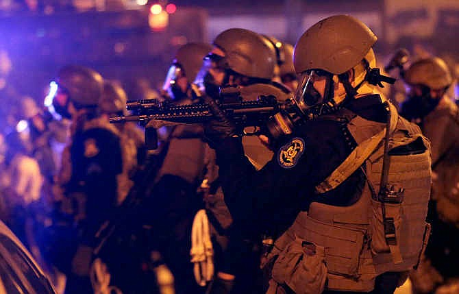 Police advance after tear gas was used to disperse a crowd Sunday, Aug. 17, 2014, during a protest for Michael Brown, who was killed by a police officer last Saturday in Ferguson, Mo. As night fell Sunday in Ferguson, another peaceful protest quickly deteriorated after marchers pushed toward one end of a street. Police attempted to push them back by firing tear gas and shouting over a bullhorn that the protest was no longer peaceful.