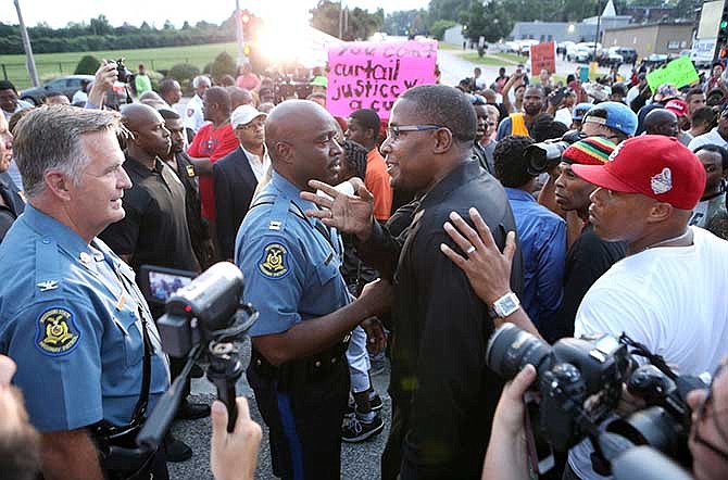 In this Aug. 16, 2014 file photo, Malik Shabazz, center, president of Black Lawyers for Justice and former chairman of the New Black Panther Party, talks with Col. Ron Replogle, left, and Capt. Ron Johnson during a march with protesters in Ferguson, Mo. Shabazz' organization and others, made up mostly of black volunteers, have taken it upon themselves to help keep the peace in Ferguson, confident the protesters are more likely to listen to them than police.