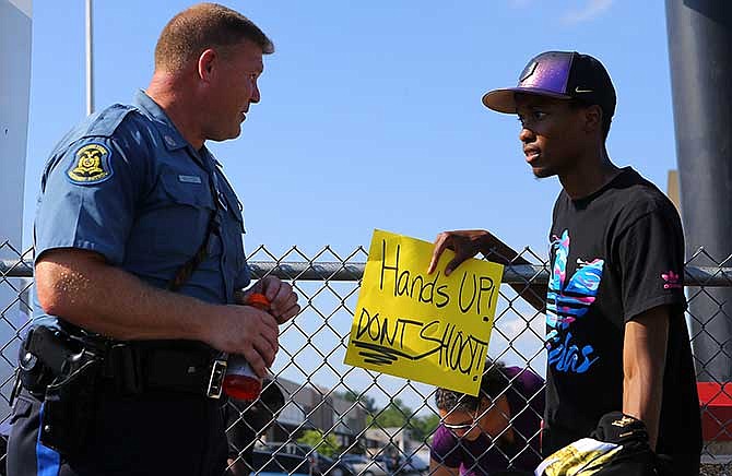 In an effort to foster some good will Missouri State Higway Patrol trooper D. Reuter chats with protester Robert Clark along West Florissant Avenue on Tuesday, Aug. 19, 2014, in Ferguson, Mo. The city of Ferguson, Missouri, says it working hard to better connect with the community and learn from the "discord and heartbreak" that followed the shooting death of 18-year-old Michael Brown by a police officer.