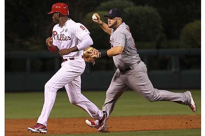 St. Louis Cardinals' Matt Adams runs past Philadelphia Phillies' Domonic Brown on a throwing error to third as Ryan Howard scores on a hit by Carlos Ruiz in the third inning of a baseball game, Friday, Aug. 22, 2014, in Philadelphia. 