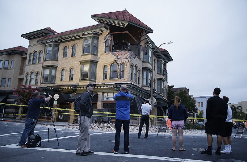 People look at a damaged building with a section of tiled roof precariously tilting over an exposed room following an earthquake Sunday in Napa, Calif.