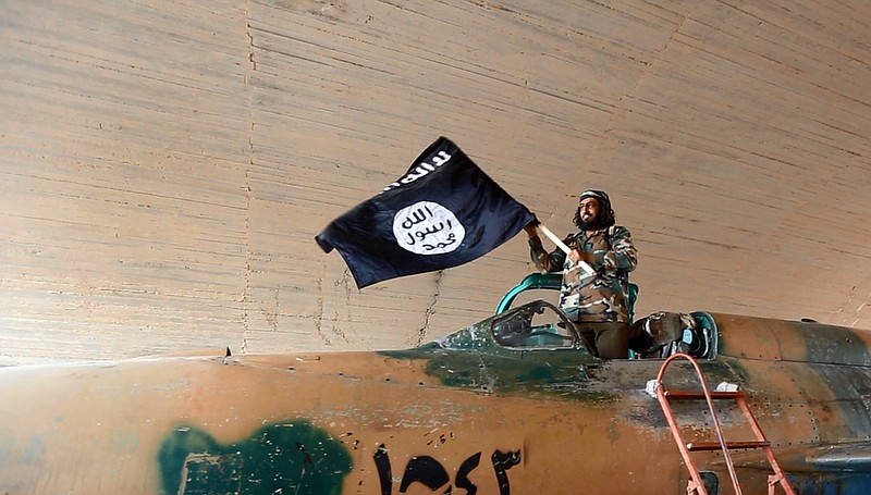 A fighter of the Islamic State group waving their flag from inside a captured government fighter jet following the battle for the Tabqa air base, in Raqqa, Syria on Sunday.   A U.N. commission on Wednesday accused the extremist Islamic State organization of committing crimes against humanity with attacks on civilians, as pictures emerged of the extremists' bloody takeover of a Syrian military air base that added to the international organization's claims.