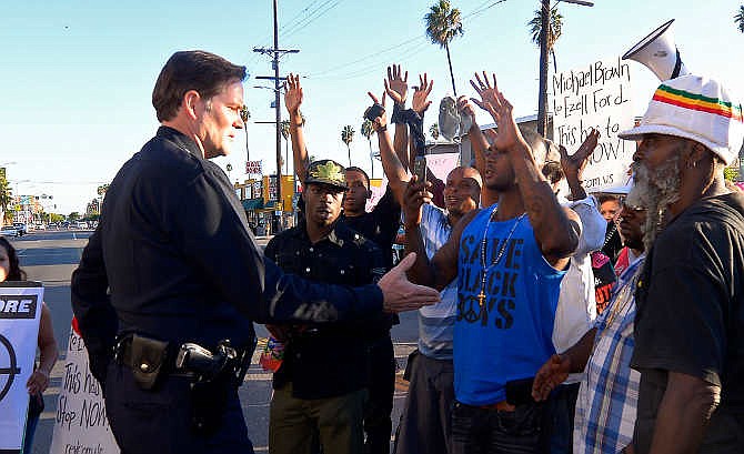 In this Aug. 14, 2014 file photo, protesters hold their hands up as a Los Angeles Police Department officer tries to talk to them in front of the 77th Street police station in Los Angeles during a protest of the LAPD shooting of Ezell Ford. Police say that Ford had attempted to remove a gun from an officer's holster on Monday when he was shot and killed, which differs from accounts by the family of the man. Details may differ, circumstances of their deaths may remain unknown, but the outrage that erupted after the Aug. 9 fatal shooting of the unarmed, black 18-year-old by a white officer in Ferguson, Missouri, has become a rallying cry in protests over police killings across the nation. 